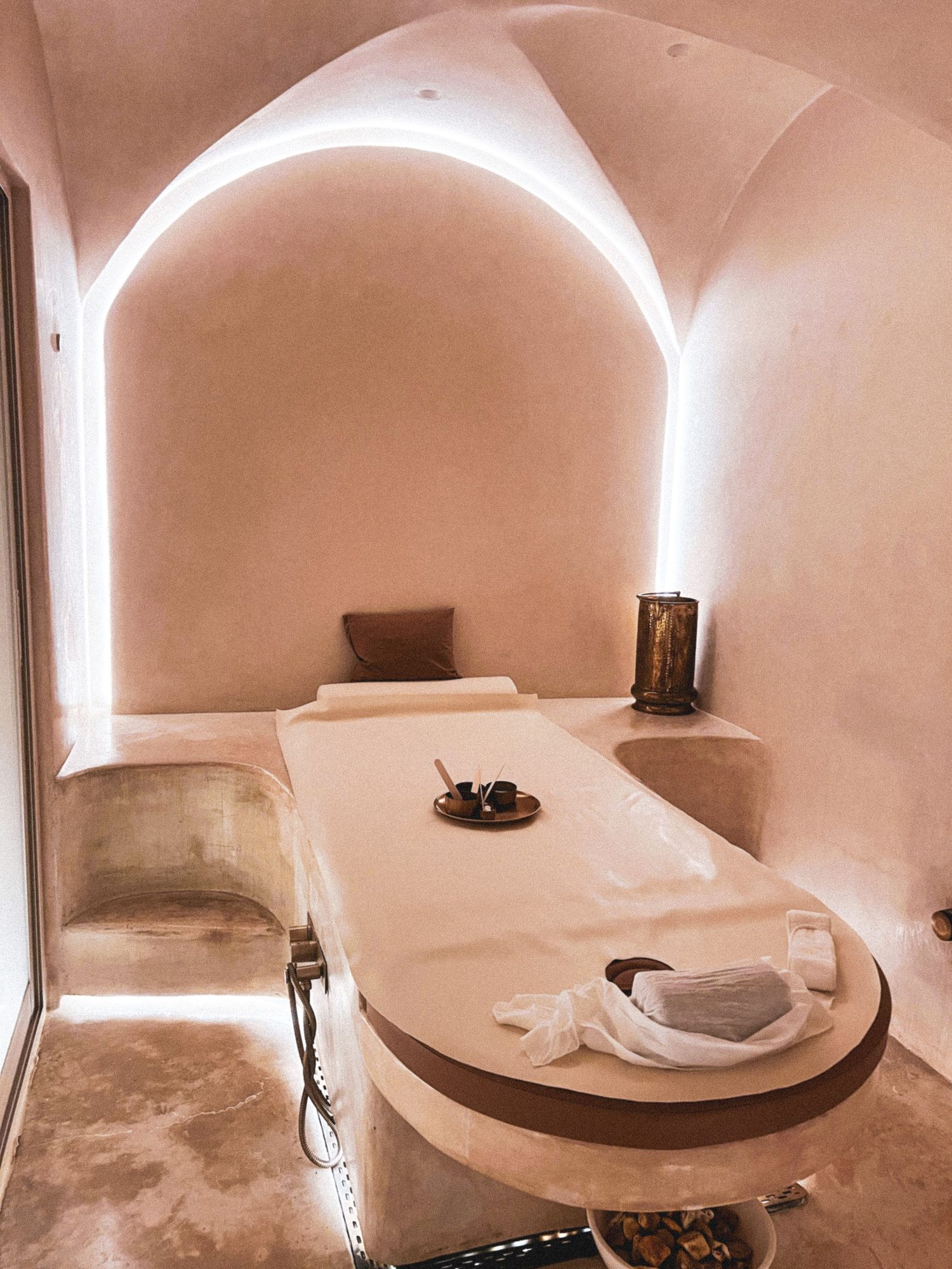 Treatment room with an arched ceiling, warm lighting and a made up massage bed