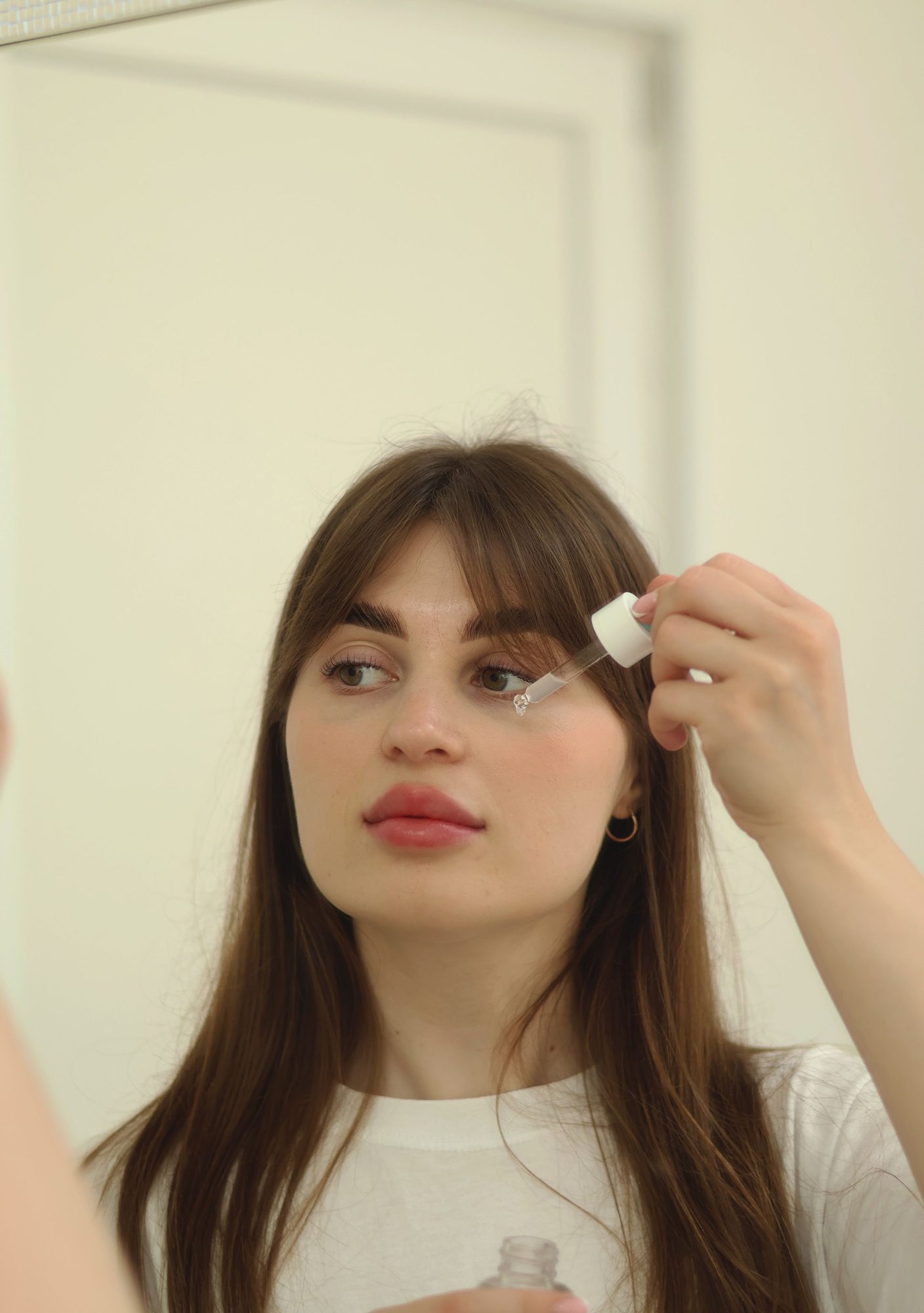 Woman applying a dropper of serum near her eyes